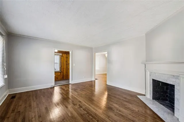 a view of an empty room with wooden floor fireplace and a window