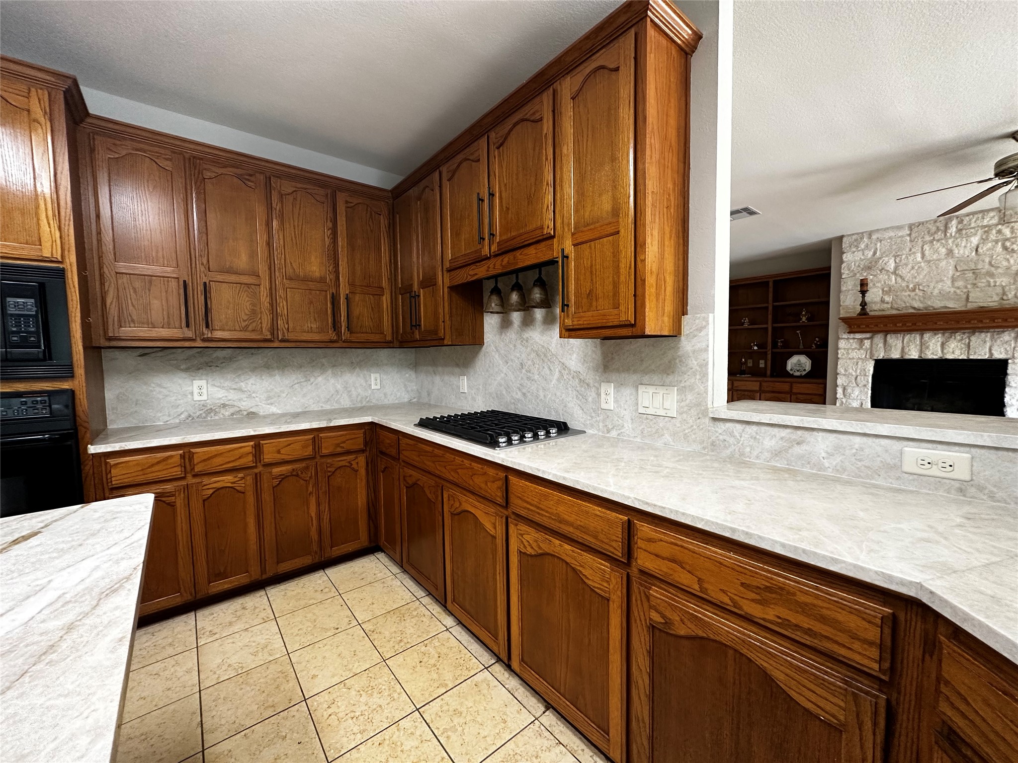 13615 Copperleaf Trail Manchaca, TX 78652 - Photo 38 of 39 Kitchen with a stone fireplace, wood finish cabinetry, black appliances, light tile patterned floors, and open floor plan