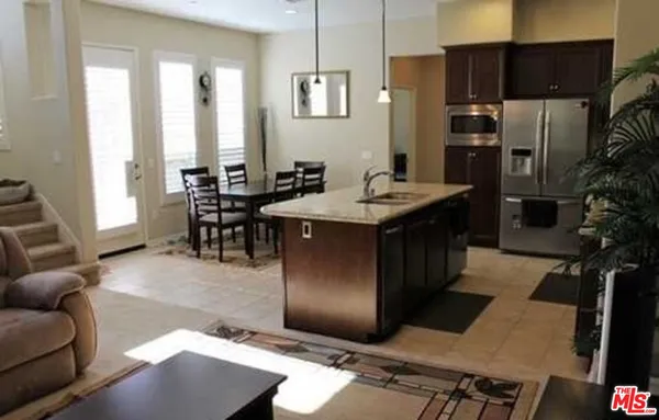 a living room with stainless steel appliances kitchen island granite countertop a table chairs and a refrigerator