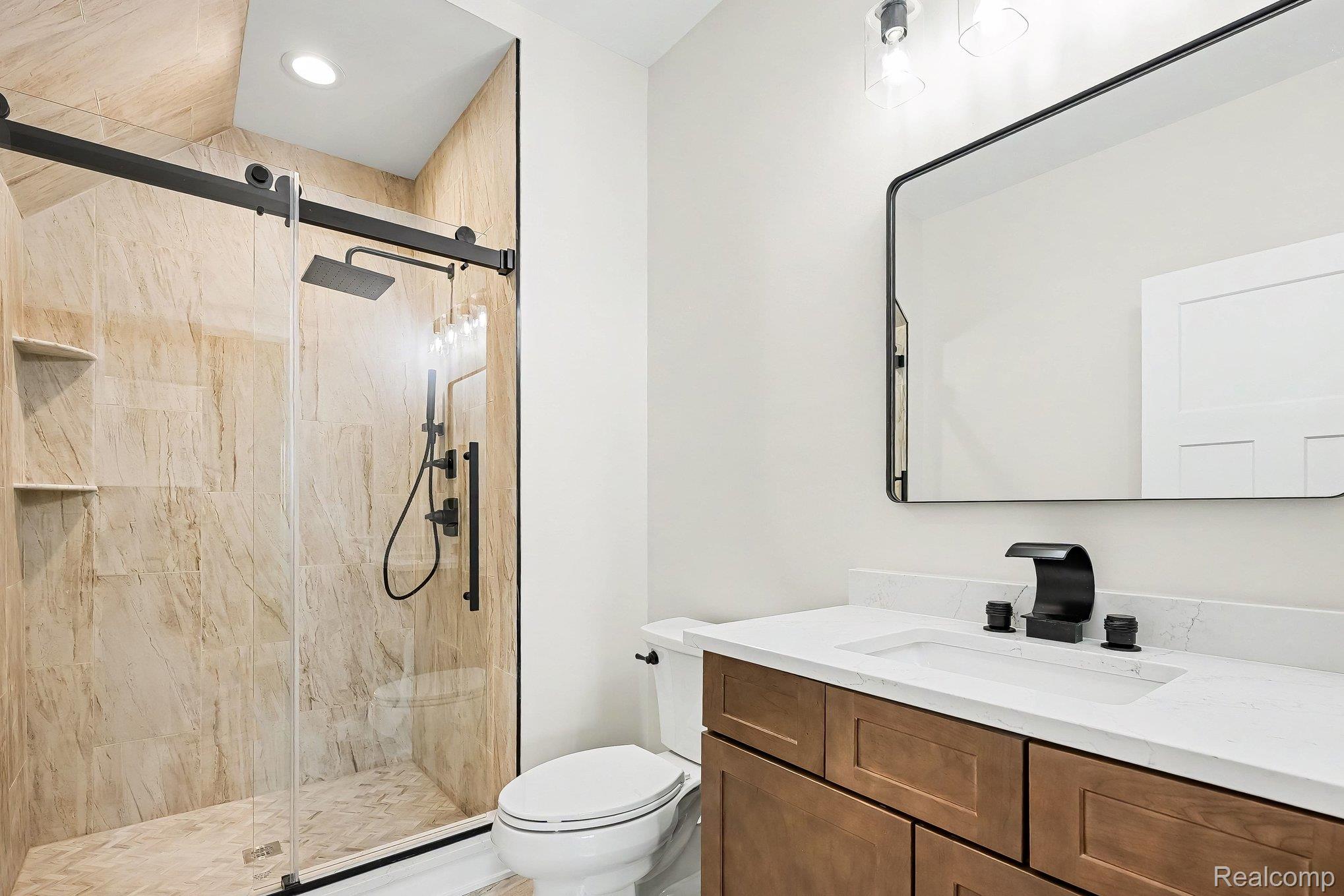57560 Omo Road Ray, MI 48096 - Photo 23 of 44 1st floor bathroom featuring a glass-enclosed shower with natural stone-finish tile, matte black fixtures, recessed lighting, and built-in shelving