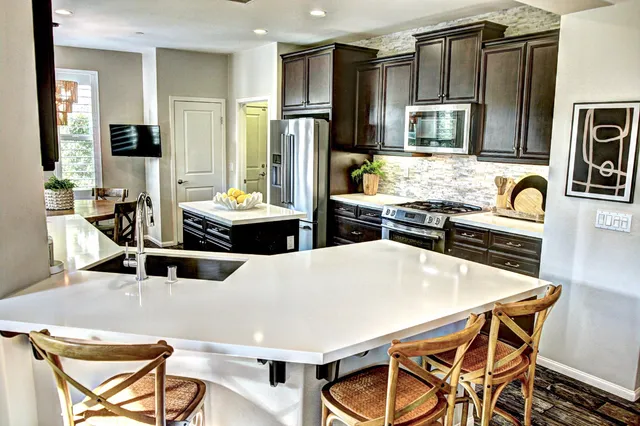 a kitchen with stainless steel appliances kitchen island granite countertop a stove a refrigerator a sink a dining table and chairs with wooden floor