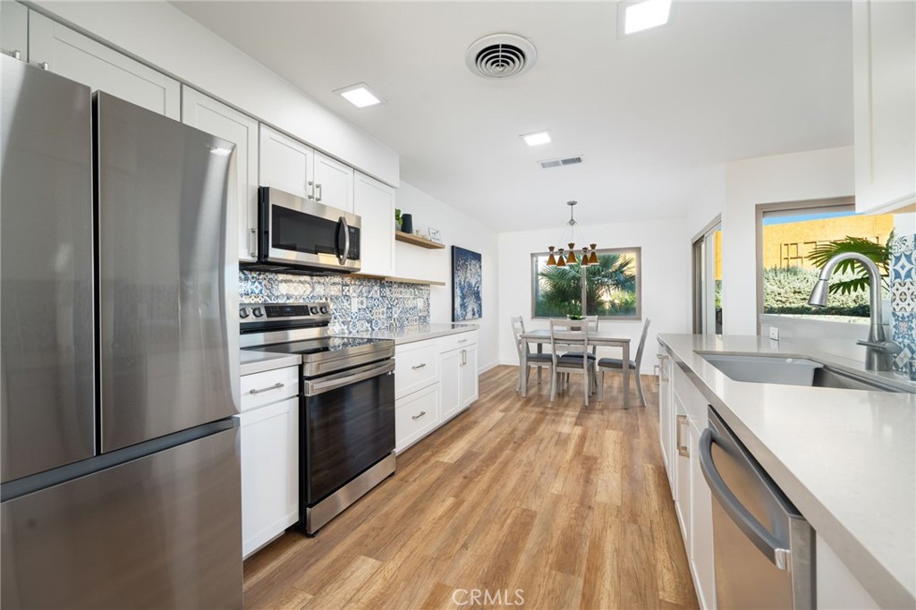 80071 Palm Cir Drive La Quinta, CA 92253 - Photo 24 of 40 a kitchen with stainless steel appliances a stove top oven a sink dishwasher a refrigerator and a dining table with wooden floor