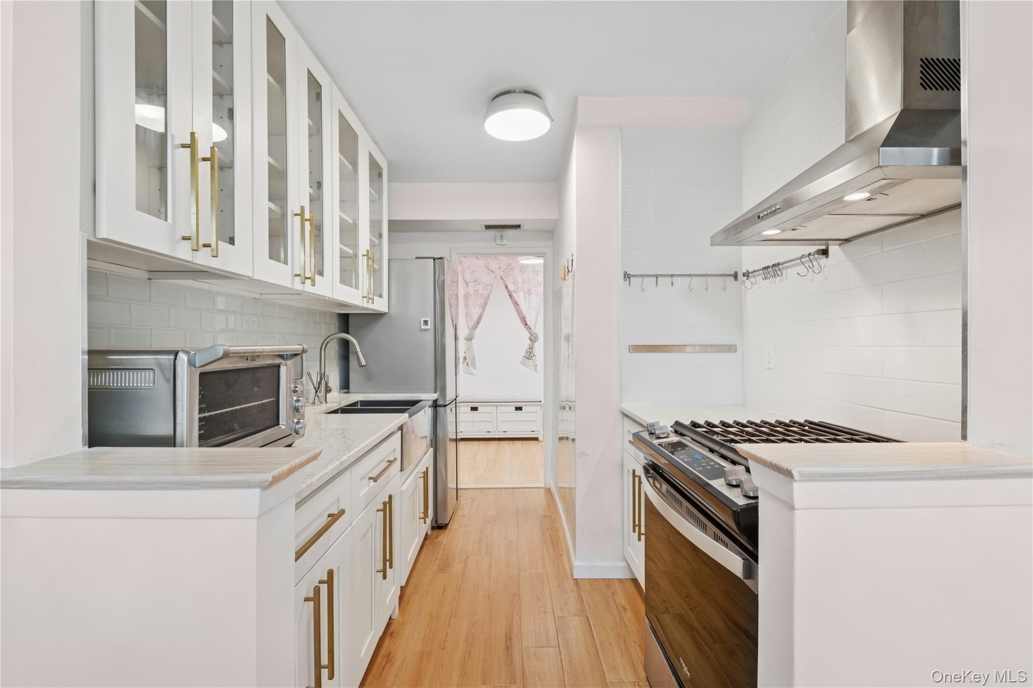 102-30 66th Road, Unit 1G Queens, NY 11375 - Photo 3 of 10 Kitchen with wall chimney exhaust hood, stainless steel gas range, decorative backsplash, light wood-type flooring, and light countertops