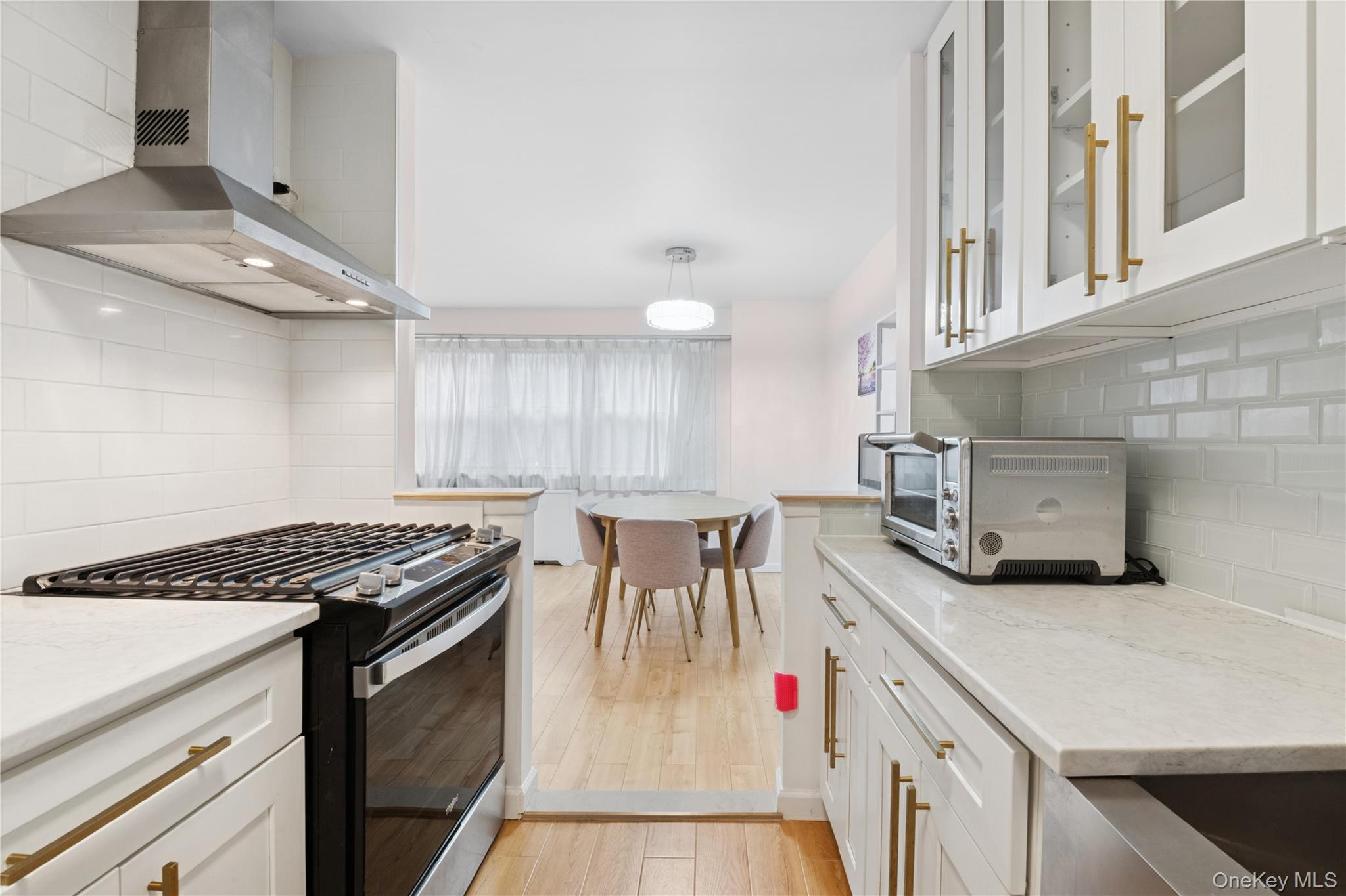102-30 66th Road, Unit 1G Queens, NY 11375 - Photo 4 of 10 Kitchen with stainless steel range with gas stovetop, wall chimney exhaust hood, backsplash, light stone countertops, and white cabinetry