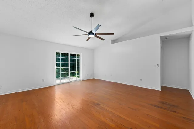 a view of an empty room with wooden floor ceiling fan and a window