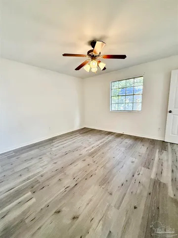 an empty room with wooden floor fan and windows