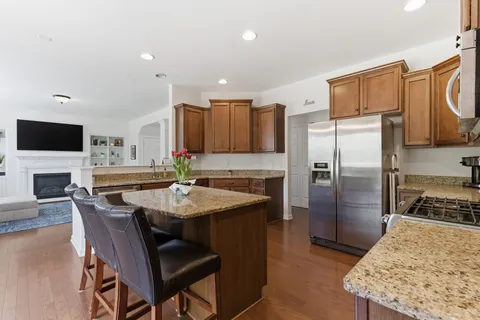 a kitchen with stainless steel appliances kitchen island granite countertop a refrigerator a stove a sink a dining table and chairs with wooden floor