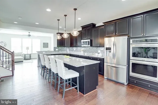 a kitchen with stainless steel appliances kitchen island granite countertop a refrigerator a stove a sink a dining table and chairs with wooden floor