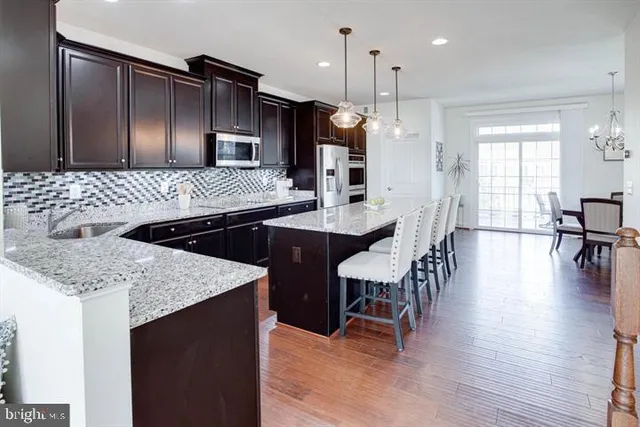 a kitchen with stainless steel appliances granite countertop a stove a refrigerator a sink a dining table and chairs with wooden floor