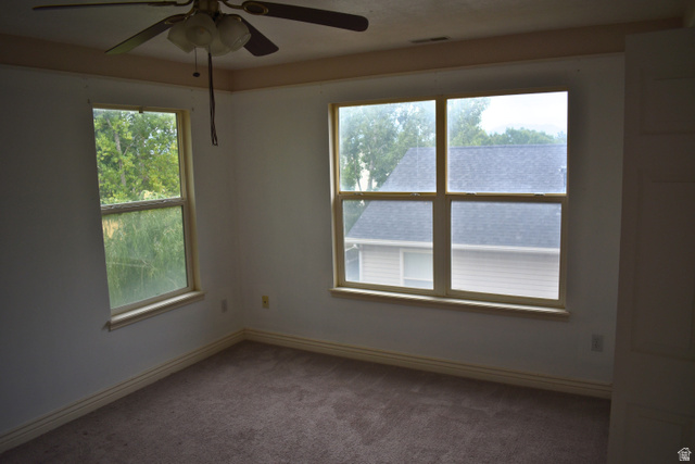3327 East Windhover Road Eagle Mountain, UT 84005 - Photo 16 of 38 Light-filled room featuring a ceiling fan, two windows with wood-finish trim, and brown carpet flooring