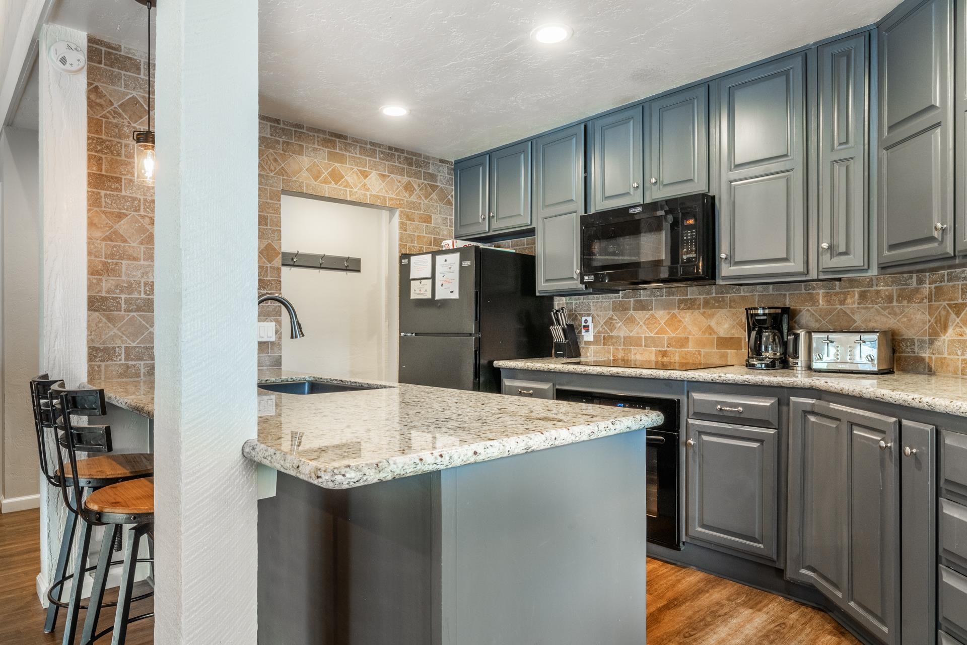 362 Old Mammoth Road, Unit 4 Mammoth Lakes, CA 93546 - Photo 8 of 50 Kitchen featuring light stone counters, gray cabinets, a kitchen bar, black appliances, and backsplash