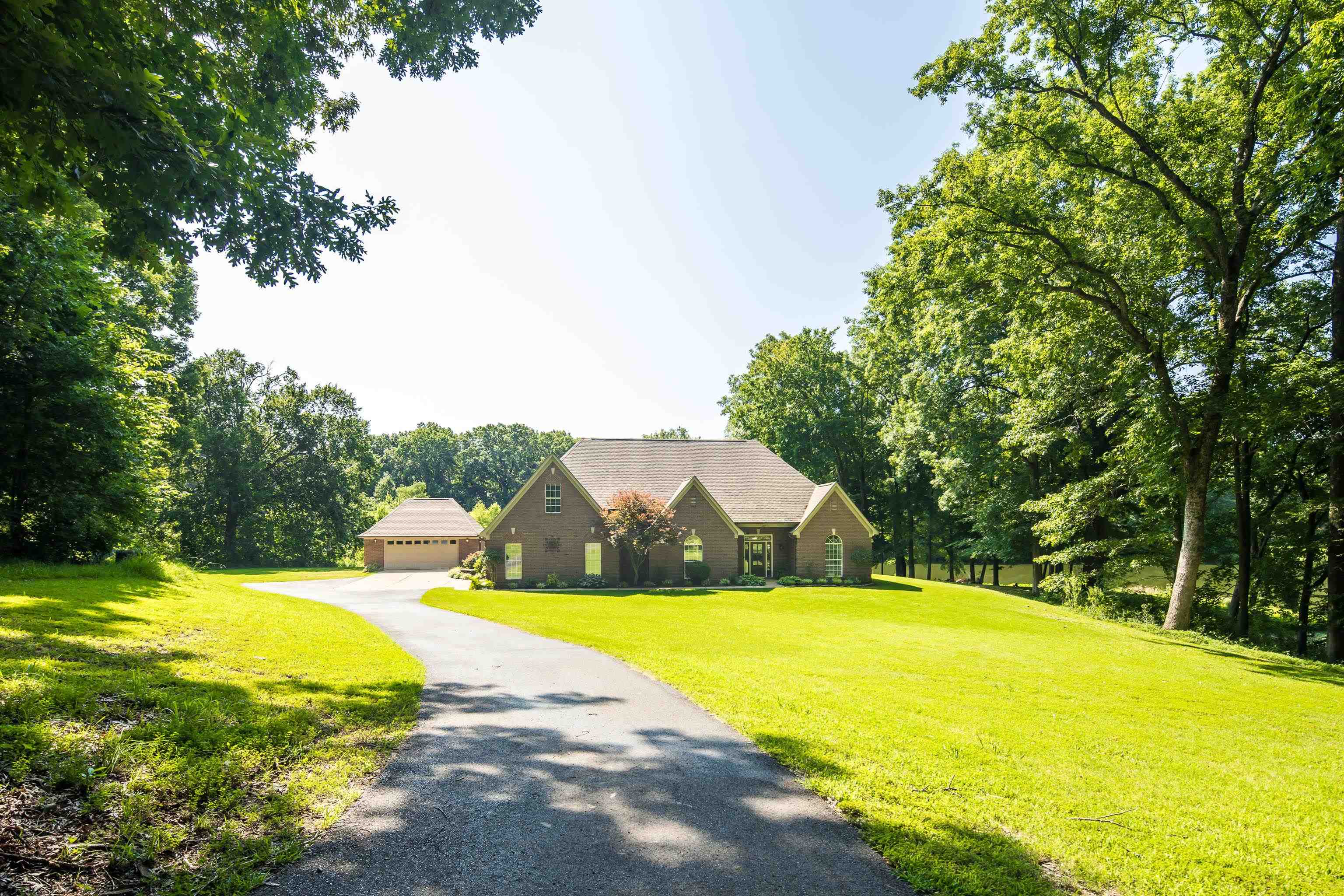243 Hayes Road Munford, TN 38058 - Photo 2 of 25 Brick exterior residence with an attached garage, featuring a long paved driveway, surrounded by mature trees and manicured lawns