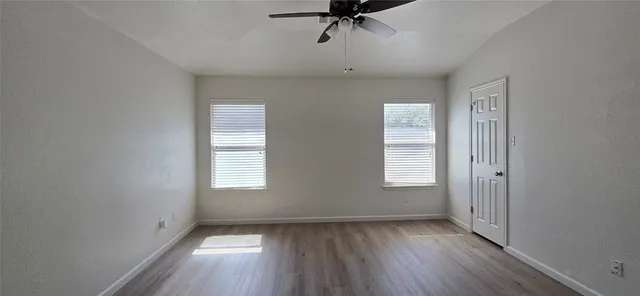 a view of empty room with wooden floor and fan