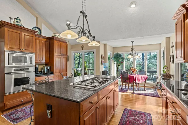 a kitchen with granite countertop a stove a sink dishwasher a dining table and chairs with wooden floor