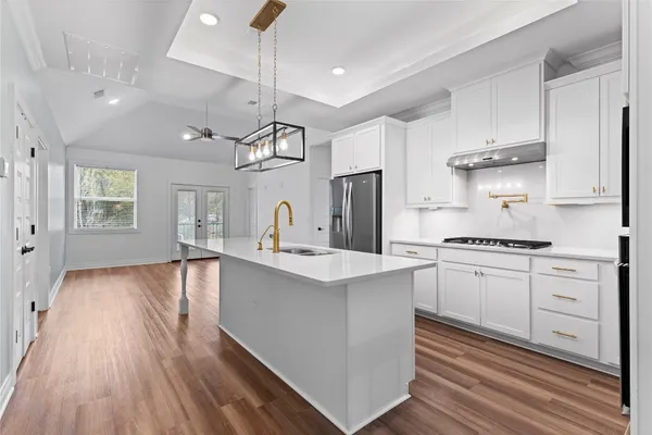 a kitchen with stainless steel appliances granite countertop a sink dishwasher a refrigerator white cabinets and wooden floor next to a window