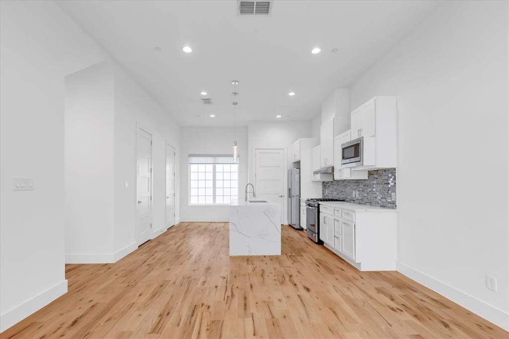 1910 Caddo Street, Unit A205 Dallas, TX 75204 - Photo 16 of 36 a open kitchen with granite countertop a stove top oven a sink and white cabinets with wooden floor