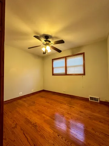 a view of an empty room with wooden floor and a chandelier fan