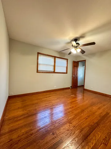 a view of an empty room with wooden floor and fan