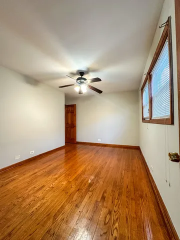 a view of an empty room with wooden floor and a ceiling fan