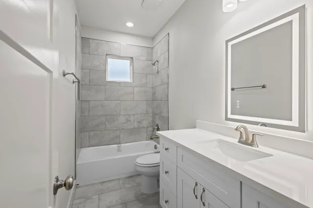 a bathroom with a granite countertop bathtub sink vanity mirror and toilet