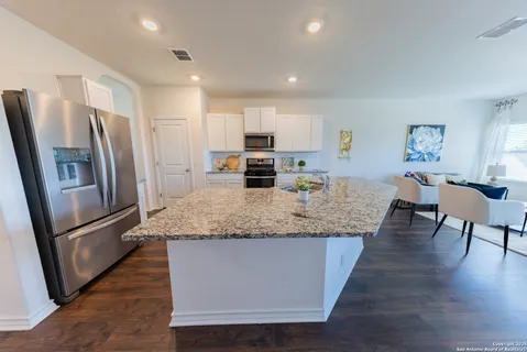 a kitchen with stainless steel appliances granite countertop a refrigerator a stove a sink a dining table and chairs with wooden floor