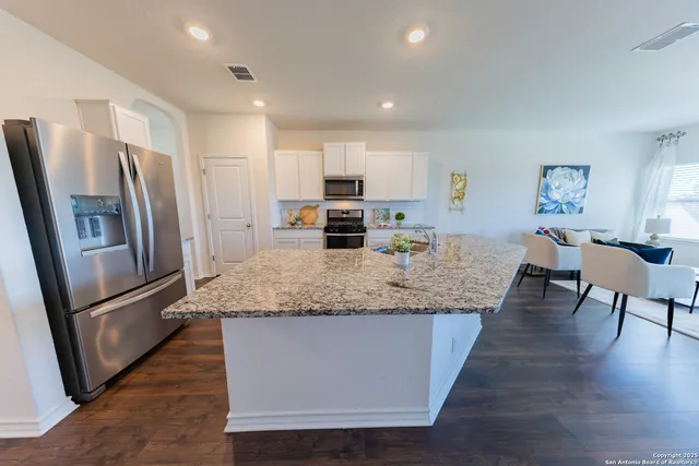 a kitchen with stainless steel appliances granite countertop a refrigerator a stove a sink a dining table and chairs with wooden floor