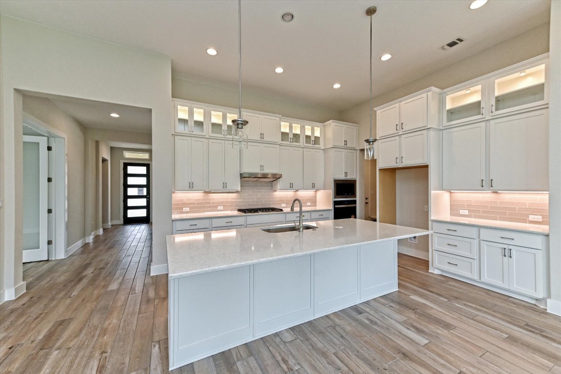 1221 Stormy Drive Georgetown, TX 78628 - Photo 2 of 33 a large white kitchen with kitchen island a stove a sink dishwasher and wooden cabinets with wooden floor