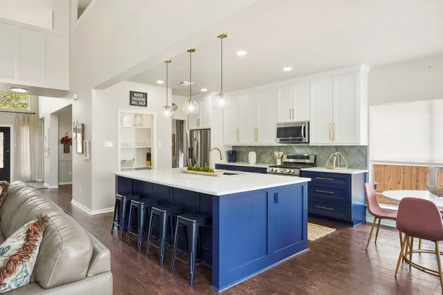 a open kitchen with stainless steel appliances granite countertop a stove top oven a sink dishwasher a dining table and chairs with wooden floor