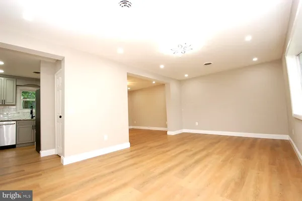 a view of an empty room with wooden floor and a kitchen view