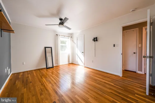a view of an empty room with wooden floor and a ceiling fan