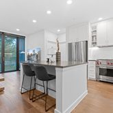 a kitchen with stainless steel appliances kitchen island granite countertop a refrigerator a stove top oven and a dining table with wooden floor