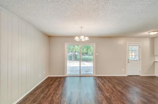 an empty room with wooden floor chandelier and windows