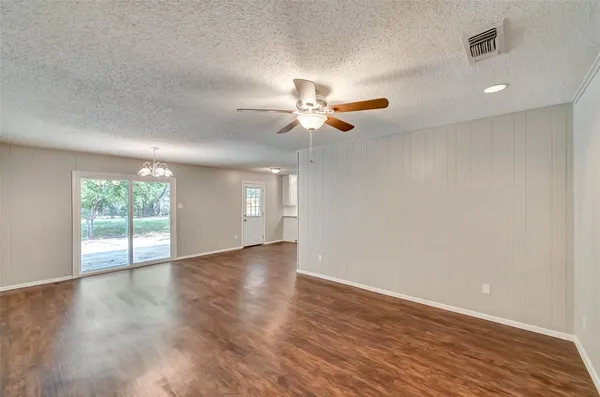 an empty room with wooden floor chandelier fan and windows