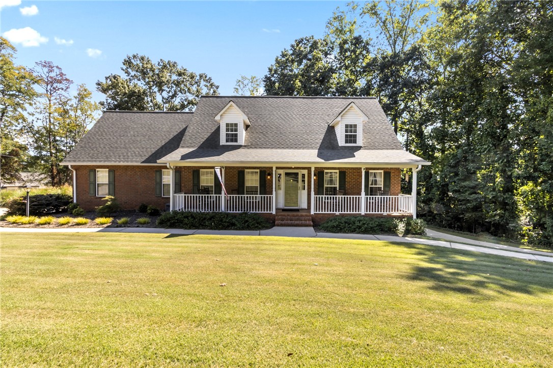 Classic brick architecture meets a welcoming front porch set against a lush, wooded backdrop.
