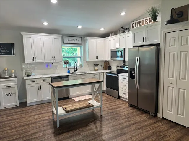 a kitchen with a refrigerator a sink dishwasher a stove and white cabinets with wooden floor