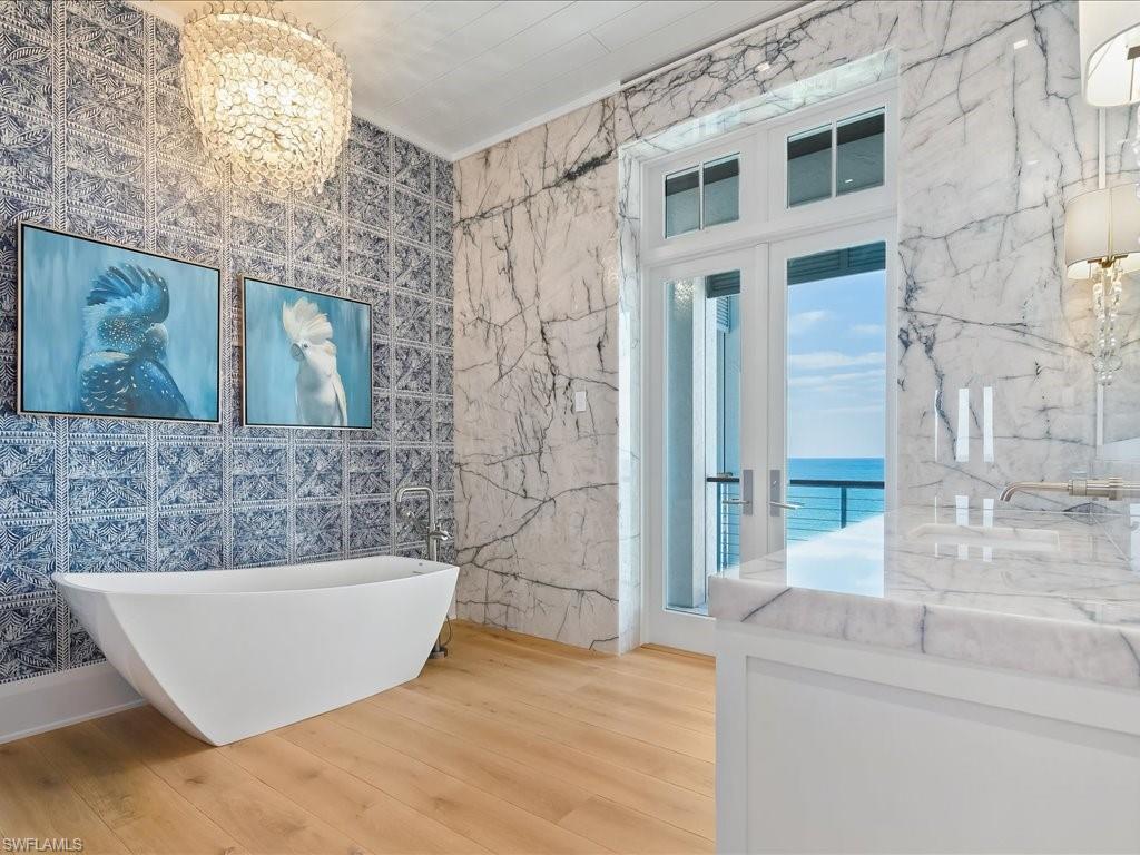 7409 Bay Colony Drive Naples, FL 34108 - Photo 22 of 46 Bathroom with tile walls, wood finished floors, a chandelier, a freestanding bath, and a water view