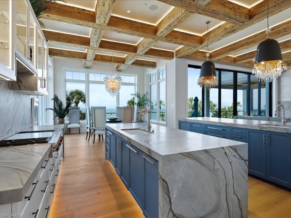 7409 Bay Colony Drive Naples, FL 34108 - Photo 29 of 46 Kitchen featuring blue cabinets, a large island with sink, decorative light fixtures, light stone countertops, and a chandelier