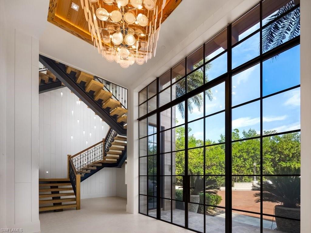 7409 Bay Colony Drive Naples, FL 34108 - Photo 43 of 46 Entryway with a wall of windows, stairs, a chandelier, and a high ceiling
