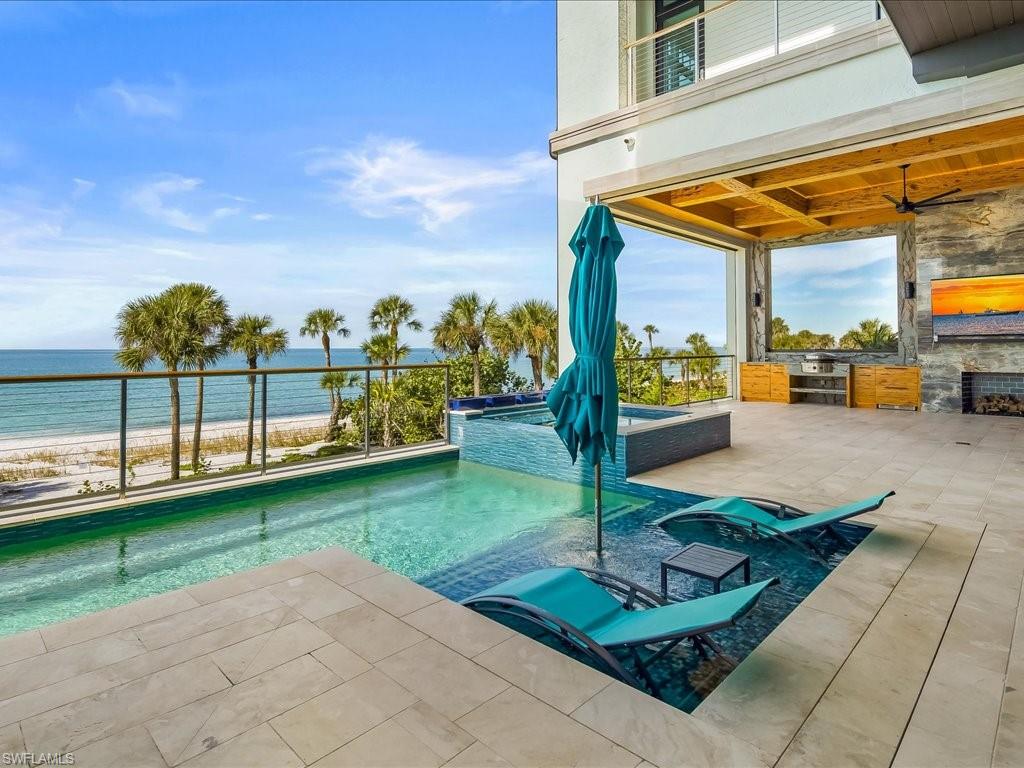 7409 Bay Colony Drive Naples, FL 34108 - Photo 6 of 46 View of pool with view of water and beach, a pool with connected hot tub, a patio area, and an outdoor kitchen