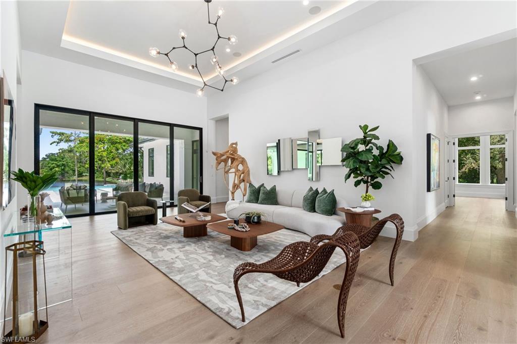 337 West Street Naples, FL 34108 - Photo 15 of 50 Living room with a towering ceiling, a raised ceiling, light hardwood / wood-style floors, and a notable chandelier