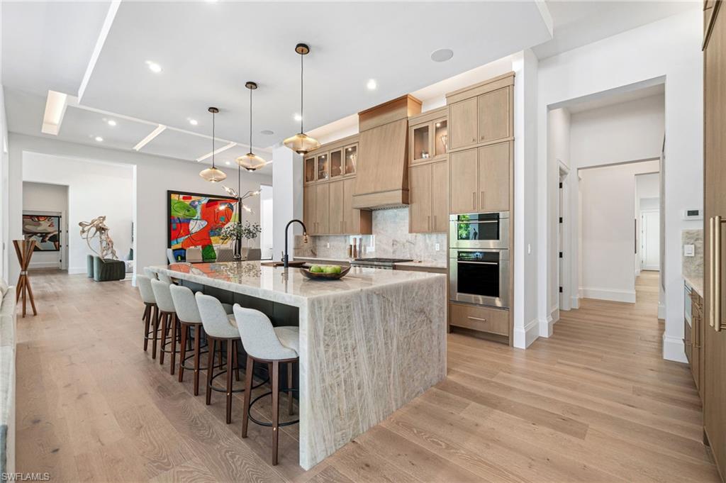 337 West Street Naples, FL 34108 - Photo 22 of 50 Kitchen featuring light hardwood / wood-style flooring, tasteful backsplash, light stone counters, decorative light fixtures, and a center island with sink