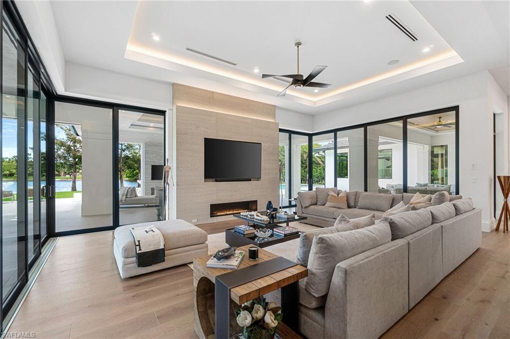 337 West Street Naples, FL 34108 - Photo 24 of 50 Living room with light wood-type flooring, a fireplace, ceiling fan, and a raised ceiling
