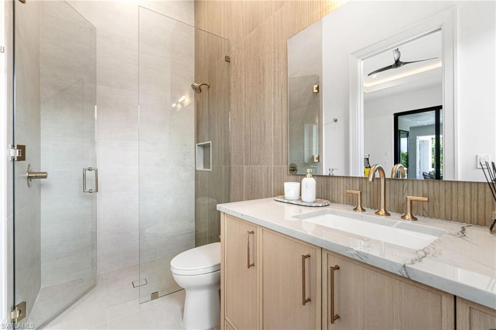 337 West Street Naples, FL 34108 - Photo 29 of 50 Bathroom featuring tile walls, tiled shower, tile patterned floors, toilet, and vanity