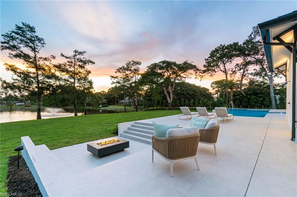 337 West Street Naples, FL 34108 - Photo 10 of 50 Patio terrace at dusk with a water view, a yard, and an outdoor fire pit
