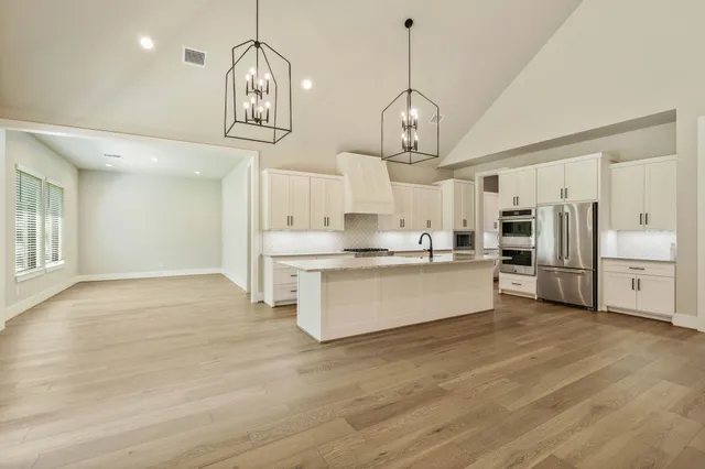 a large kitchen with stainless steel appliances kitchen island a large island a stove a refrigerator cabinets and chandelier