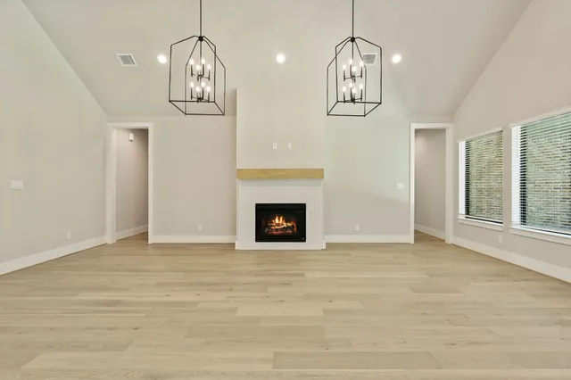 a view of an empty room with chandelier fireplace and wooden floor
