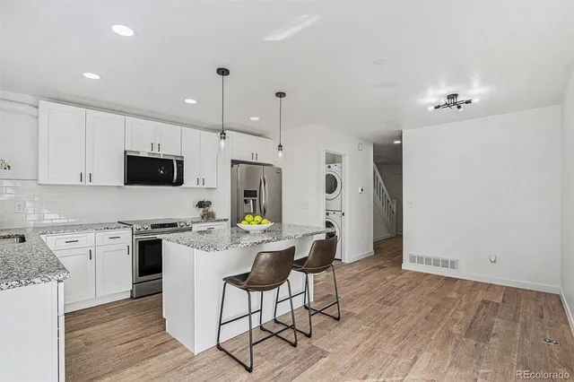 a kitchen with stainless steel appliances a stove top oven a refrigerator a sink and white cabinets with wooden floor