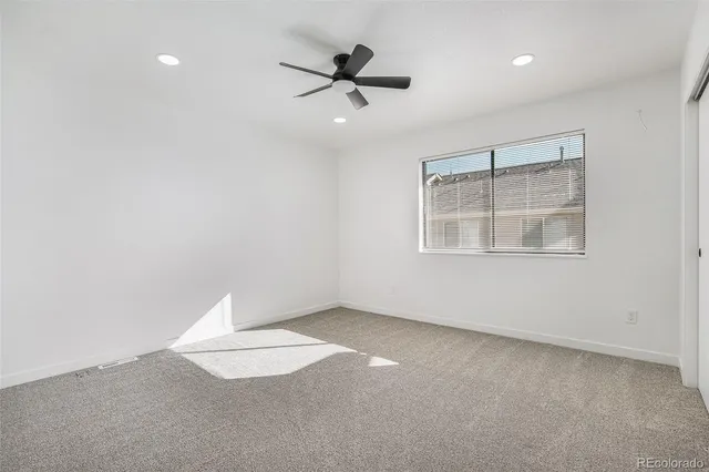 an empty room with ceiling fan and windows