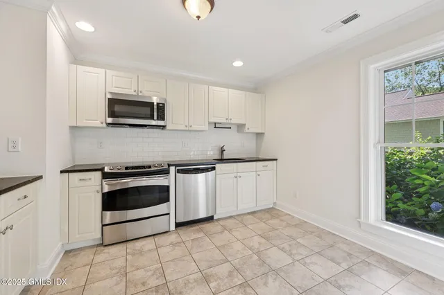 a kitchen with granite countertop white cabinets stainless steel appliances and a window