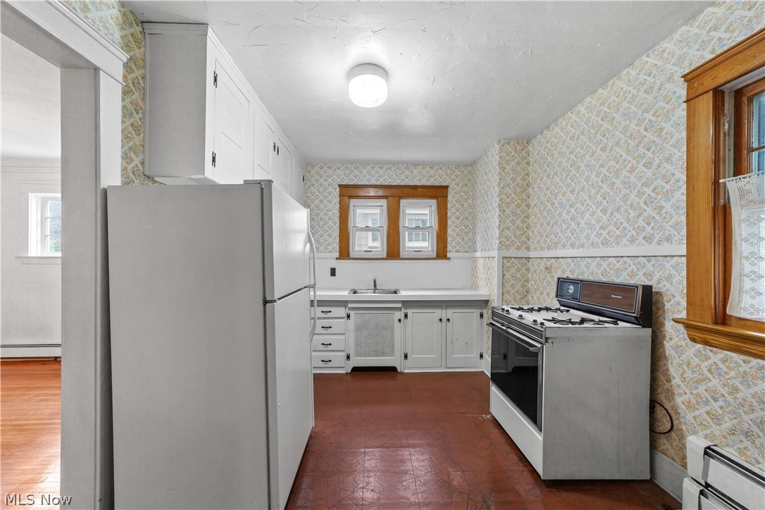 Kitchen with a baseboard heating unit, dark wood-type flooring, white cabinets, and white appliances
